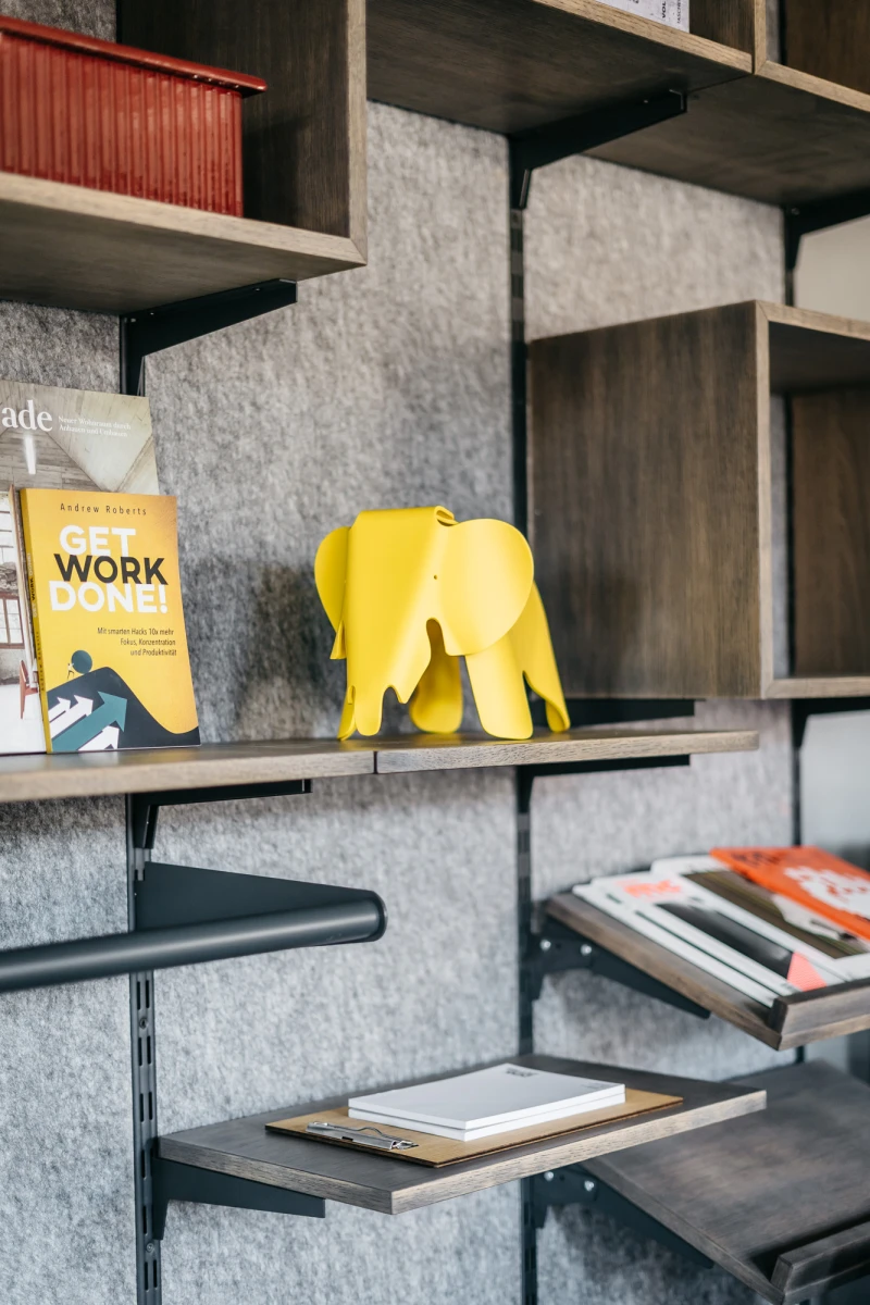 Bunte Elefantenfigur auf einem Regal mit B&uuml;chern und Notizen.