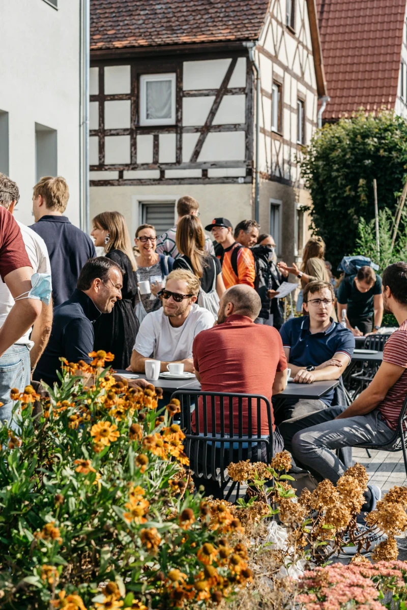 Menschen genie&szlig;en Kaffee und Gespr&auml;che im Freien vor dem Schwarzen Adler.
