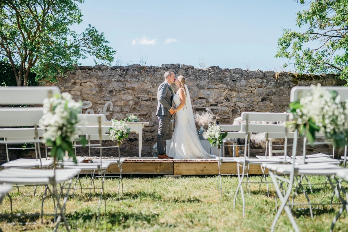 Hochzeitspaar k&uuml;sst sich vor romantischer Kulisse im Freien.